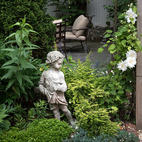 A figure in stone standing within a mixed planting bed